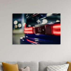 May include: Close-up of a blue car's rear end, showcasing the taillight and a portion of the spoiler. The taillight glows red, contrasting with the dark blue paint. The image is a detail shot of a vehicle.