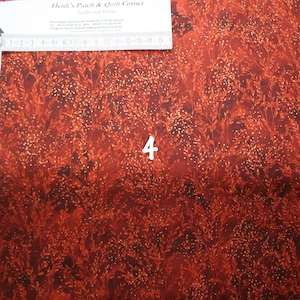 May include: A close-up of a red fabric with a gold glitter pattern. The fabric has a subtle leaf design and the text "Heidi's Patch & Quilt Corner" is visible in the top left corner.