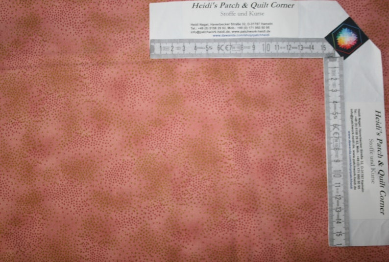 May include: A close-up of a pink fabric with a subtle pattern of small gold dots. A ruler is visible in the top right corner of the image. The ruler is marked in centimeters and inches.