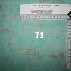 Könnte beinhalten: Nahaufnahme eines türkisfarbenen Stoffes mit der weißen Nummer "73" darauf gedruckt. Im Hintergrund sind ein weißes Lineal und eine Visitenkarte für Heidi's Patch & Quilt Corner zu sehen.