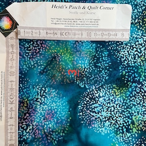 Op de afbeelding: Een close-up van een tealblauwe stof met een wit, blauw en groen gespikkeld patroon. De stof wordt gemeten met een liniaal in centimeters. De tekst "Heidi's Patch & Quilt Corner" is zichtbaar in de rechterbovenhoek van de afbeelding.