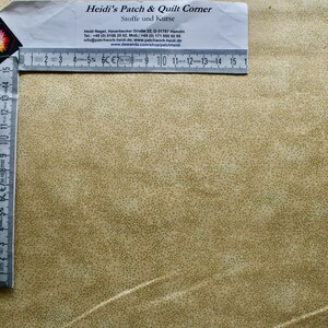 Könnte beinhalten: Ein weißes Lineal mit schwarzen Markierungen liegt auf einem beigefarbenen Stoff mit einem gesprenkelten Muster. Das Lineal ist mit Zahlen von 1 bis 15 beschriftet. Der Stoff ist mit "Heidi's Patch & Quilt Corner" und "Stoffe und Kurse" beschriftet.