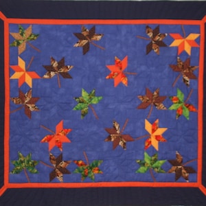 Può includere: Una trapunta blu con un design a patchwork di foglie d'acero colorate. Le foglie sono disposte in modo casuale e sono realizzate con tessuti diversi. La trapunta è bordata con un bordo blu scuro e arancione.