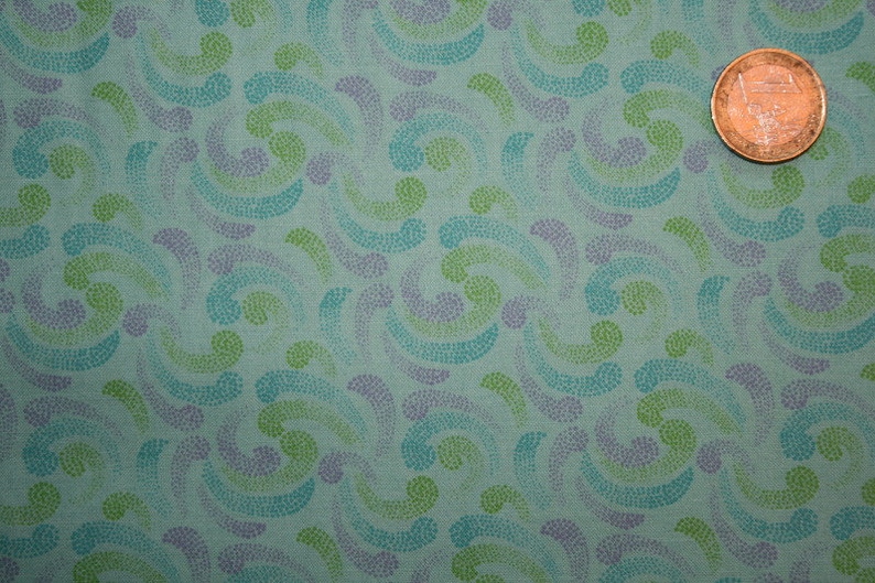 May include: A light teal fabric featuring a repeating pattern of dotted swirls in shades of blue, green, and purple. A coin is placed on the fabric for scale. The fabric has a textured appearance.