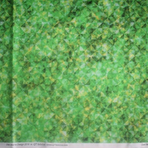 Op de afbeelding: Groene stof met een geometrisch patroon van overlappende driehoeken. De stof heeft een subtiele, textuur en een licht vervaagde uitstraling. De tekst "Dan Morris Design 2019 for QT Fabrics www.QTfabrics.com" is onderaan de afbeelding gedrukt.