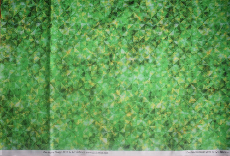 Op de afbeelding: Groene stof met een geometrisch patroon van overlappende driehoeken. De stof heeft een subtiele, textuur en een licht vervaagde uitstraling. De tekst "Dan Morris Design 2019 for QT Fabrics www.QTfabrics.com" is onderaan de afbeelding gedrukt.