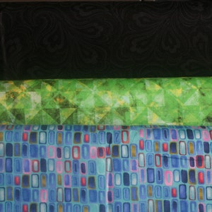 Op de afbeelding: Drie stofstalen, een zwart met een draaiend patroon, een groen met een geometrisch patroon en een blauw met een geometrisch patroon van rechthoeken.