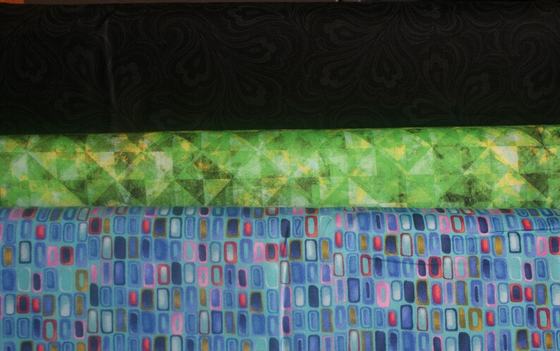 Op de afbeelding: Drie stofstalen, een zwart met een draaiend patroon, een groen met een geometrisch patroon en een blauw met een geometrisch patroon van rechthoeken.