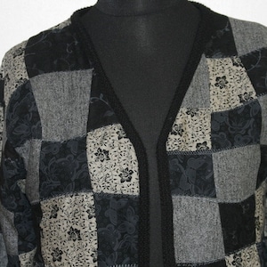 May include: A black and gray patchwork cardigan with a floral pattern. The cardigan has a V-neck and a long sleeve.