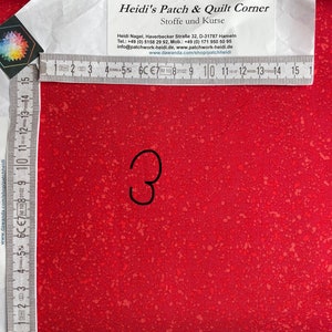 May include: A close-up of a red fabric with a speckled pattern. The fabric is measured with a ruler, showing a measurement of 7.6 cm.