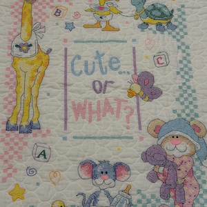 May include: A white quilted fabric featuring cross-stitched illustrations of a giraffe, a duck, a turtle, a butterfly, a mouse, and a bear. The center text reads "Cute... or WHAT?" surrounded by colorful alphabet blocks, stars, and hearts.