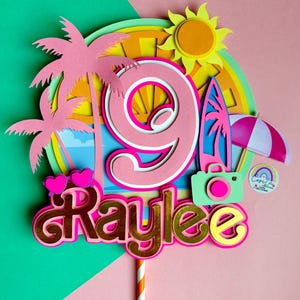May include: A vibrant cake topper with a beach theme. It features a large pink number 9, the name "Kaylee" in gold, palm trees, a surfboard, and a camera. The background includes a sun, umbrella, and a rainbow. The topper is on a striped orange and white stick.
