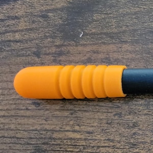 May include: A black stylus with an orange tip. The stylus has a cylindrical body and a textured orange grip. The tip is rounded, and the body is a matte black. The stylus is designed for use with touch screen devices.