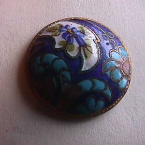 May include: A blue and white enamel button with a floral design. The button is oval shaped and has a gold rim.