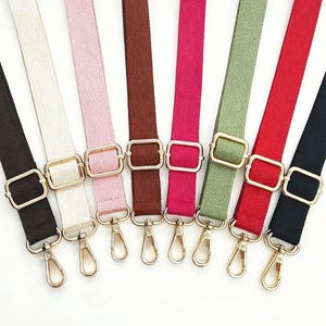 May include: Assortment of colorful bag straps in various shades, including black, white, pink, brown, fuchsia, green, red, and navy. Each strap features gold-toned metal hardware, including rectangular buckles and swivel clasps for easy attachment.