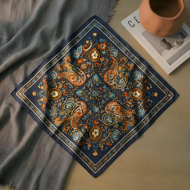 May include: A navy blue square scarf with an intricate paisley pattern in shades of orange, blue, and white. The scarf features a detailed floral design and a decorative border. This accessory is suitable for various styles.