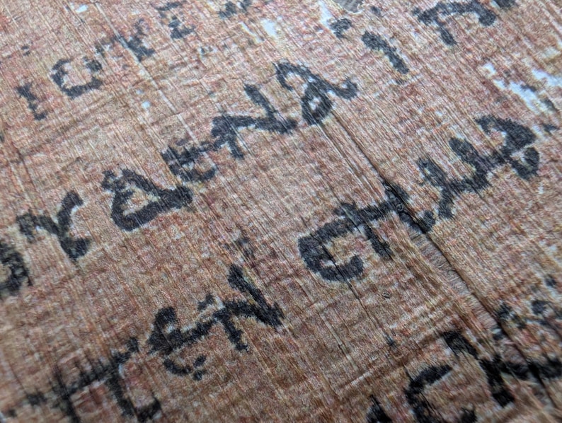 May include: Close-up of an ancient papyrus scroll with faded brown and tan tones. The papyrus has visible fibers and is inscribed with black, stylized text. The text appears to be in an ancient script, possibly hieroglyphs or a similar form of writing.
