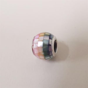 May include: A round bead with a mosaic design. The bead is made of small, square-shaped pieces in pastel colors, including pink, yellow, and green. The bead has a silver-colored metal band around the holes.