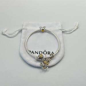 May include: A silver Pandora bracelet with a Mickey Mouse clasp and charm. The bracelet features a gold-colored Mickey Mouse head clasp and several charms, including a gold-colored carriage and a charm with a cartoon character.