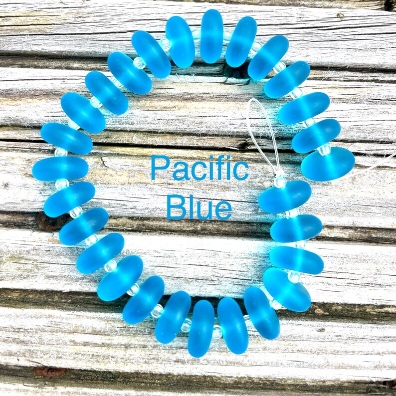 May include: A bracelet with oval, translucent, Pacific Blue beads. The beads are strung together with small, clear beads. The text "Pacific Blue" is displayed in the centre of the image.