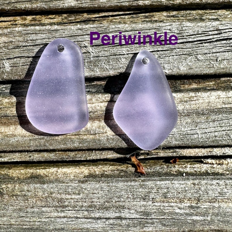 May include: Two periwinkle-coloured, teardrop-shaped pendants with small holes at the top. The pendants are displayed on a weathered wooden surface. The word "Periwinkle" is written in purple text.