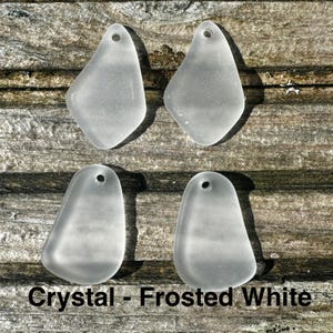 May include: Four frosted white crystal pendants, each with a teardrop shape and a small hole for threading. They are arranged on a weathered wooden surface. The text "Crystal - Frosted White" is visible at the bottom.