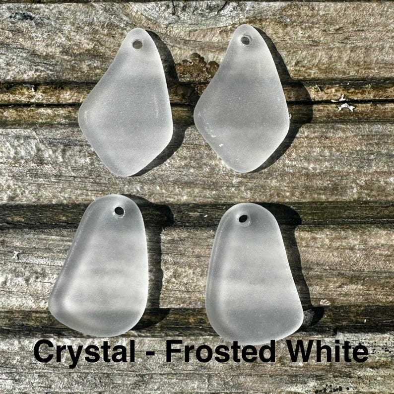May include: Four frosted white crystal pendants, each with a teardrop shape and a small hole for threading. They are arranged on a weathered wooden surface. The text "Crystal - Frosted White" is visible at the bottom.