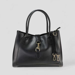 Può includere: Una borsa in pelle nera dal design strutturato. La borsa presenta due manici superiori e una tracolla staccabile. Dettagli dorati impreziosiscono la chiusura frontale a patta e gli attacchi della tracolla.