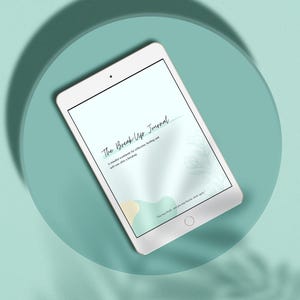 Könnte beinhalten: Ein weißes Tablet mit "The Break Up Journal" auf dem Bildschirm. Das Journal ist ein achtsames Arbeitsbuch für Reflexion, Heilung und Selbstfürsorge nach einer Trennung. Das Tablet liegt auf einer türkisfarbenen Oberfläche.