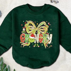 May include: A dark green sweatshirt featuring the word "GRINCHY" in a festive, colorful design. The design includes a large bow, snowflakes, and a Grinch character wearing a Santa hat. Christmas-themed apparel.