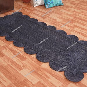 以下が含まれることがあります： ネイビーブルーのジュートランナーラグ、スカラップエッジ付き。 ラグは長方形で、織り込まれたテクスチャです。木製の床に展示されています。 装飾的な家のアクセントです。