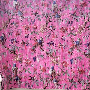 May include: A bright pink quilt featuring a repeating pattern of birds perched on branches with red and purple flowers and green leaves. The fabric has visible white running stitch quilting lines throughout the entire surface of the textile.