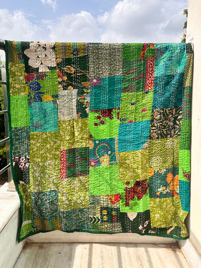 May include: A patchwork quilt with a vibrant mix of green hues, including lime, emerald, and forest green. The quilt features a variety of floral and geometric patterns, creating a textured and visually appealing design. The quilt is displayed outdoors, with a clear sky in the background.