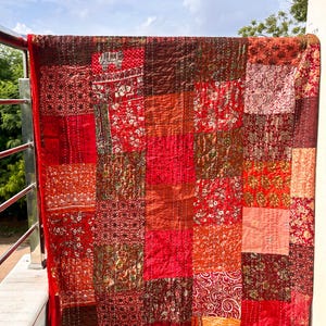 Peut inclure: Une courtepointe patchwork aux tons rouges variés, allant du cramoisi profond aux nuances écarlates plus claires. La courtepointe présente divers motifs floraux et géométriques, cousus ensemble avec des coutures visibles. Elle est bordée d'un liseré rouge.