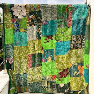 Könnte beinhalten: Ein Patchwork-Quilt in verschiedenen Grüntönen, von hell bis dunkel. Der Quilt besteht aus Quadraten aus verschiedenen Stoffen, die jeweils ein eigenes Muster haben, darunter Blumen- und geometrische Designs. Die Kanten sind mit einem dunkelgrünen Rand versehen.