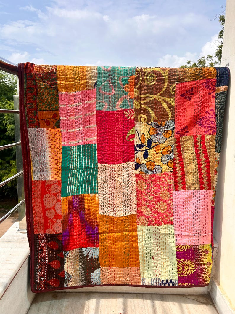May include: A patchwork quilt with a variety of colorful fabric squares. The quilt features a mix of floral, patterned, and solid fabrics in shades of red, orange, green, and pink. The edges are finished with a dark red border.