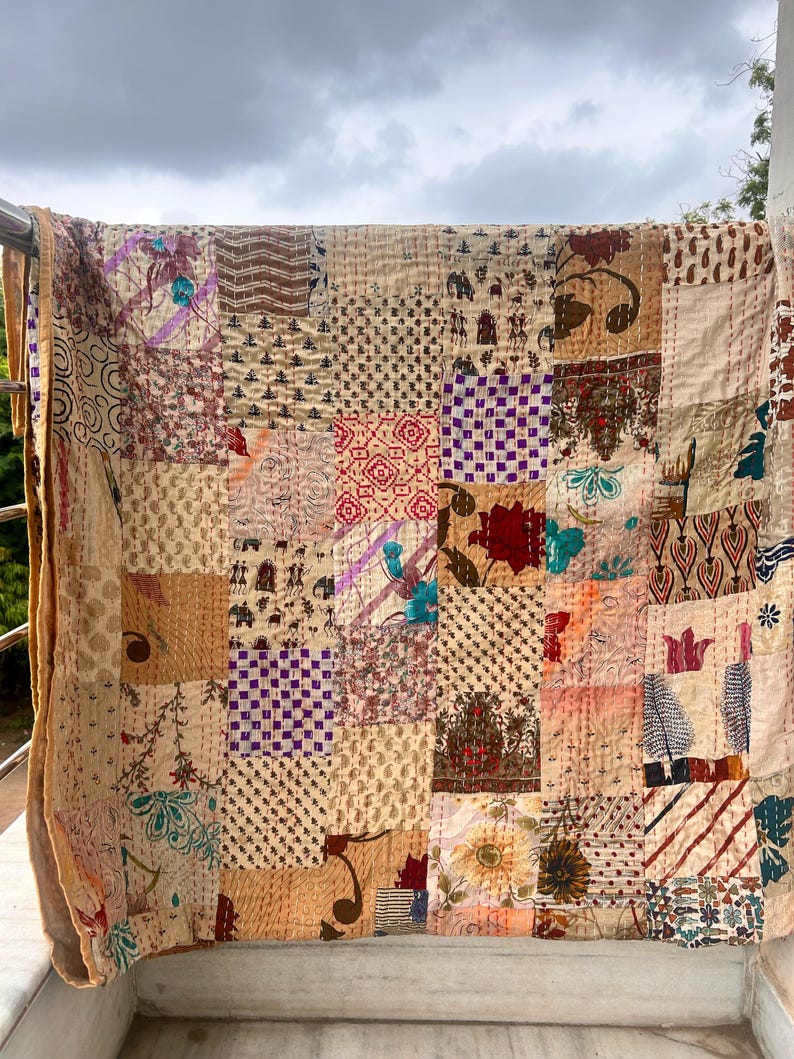 May include: A patchwork quilt with a variety of patterned squares in beige, brown, and muted colors. The quilt is draped over a railing, showcasing its intricate stitching and diverse fabric designs. The overall aesthetic is vintage and handcrafted.