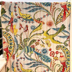 Könnte beinhalten: Cremefarbenes Textil mit einem Muster aus Vögeln und floralen Elementen in Rot, Gelb, Blau und Grün. Das Textil, möglicherweise eine Steppdecke oder ein Überwurf, weist sichtbare Nähte auf.