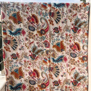 Peut inclure: Une courtepointe blanche ornée d'un motif floral et cachemire coloré. Le design comprend des nuances de rouge, de bleu, d'orange et d'or. La courtepointe est suspendue, mettant en valeur ses détails et ses coutures.
