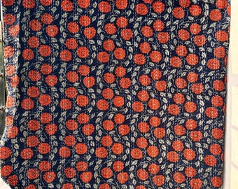 May include: A navy blue floral quilt with a repeating pattern of orange flowers and light green leaves. The quilt is hand-stitched with white thread, and is hanging outside against a blue sky.