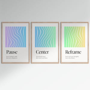 May include: Three framed art prints with inspirational text. Each print features a colorful, wavy design in shades of purple, blue, and green. The text includes the words "Pause", "Center", and "Reframe", with additional motivational phrases.