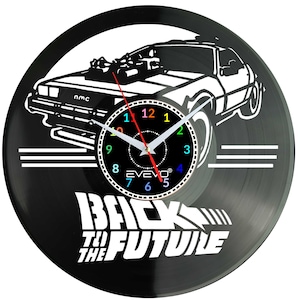 Può includere: Orologio in vinile nero con il contorno bianco di un'auto DeLorean del film "Ritorno al futuro". Il quadrante dell'orologio ha uno sfondo nero con numeri colorati e lancette bianche. Il testo "BACK TO THE FUTURE" è visualizzato in basso.
