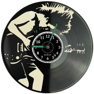 Könnte beinhalten: Eine schwarze Vinyl-Schallplattenuhr mit der Silhouette eines Gitarristen. Das Zifferblatt ist weiß mit schwarzen Zahlen und grünen Zeigern. Ein einzigartiger Dekorationsartikel.