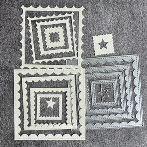 May include: A collection of square die cuts in various sizes, featuring scalloped edges and nested frames. Some have star cutouts, others have intricate patterns. The color is a light gray and white.