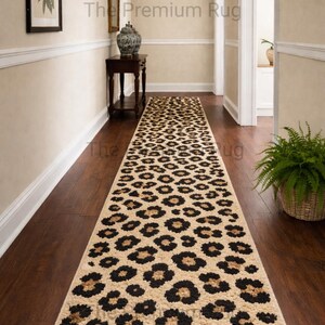 Op de afbeelding: Een lange, rechthoekige loper met een luipaardprint. De loper heeft een beige achtergrond met zwarte en bruine vlekken. De tekst "The Premium Rug" is zichtbaar. De loper ligt in een gang met een donkere houten vloer.