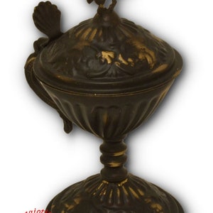May include: A gold-toned metal incense burner with a cross on top and intricate floral designs. The burner has a lid with a handle and sits on a pedestal base.