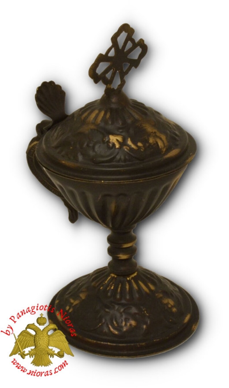 May include: A gold-toned metal incense burner with a cross on top and intricate floral designs. The burner has a lid with a handle and sits on a pedestal base.