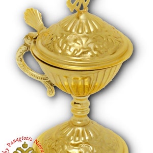 May include: A gold metal censer with a decorative floral design and a cross on top. The censer has a handle and a base with a floral design.