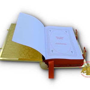 Puede incluir: Un libro encuadernado en cuero rojo con bordes dorados, con una p&aacute;gina blanca abierta. La p&aacute;gina tiene las palabras "The Holy Gospel" impresas en negro. El libro est&aacute; apoyado sobre una superficie dorada.