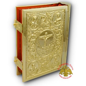 Puede incluir: Una cubierta de libro dorada en relieve con un interior rojo. La cubierta presenta una cruz con una figura de Jesucristo, rodeada de dise&ntilde;os florales y cuatro figuras m&aacute;s peque&ntilde;as. El texto "by Panagias Nioras www.nioras.com" es visible en la esquina inferior derecha.